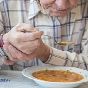 Oudere die soep eet met een lepel die geschikt is voor iemand met parkinson