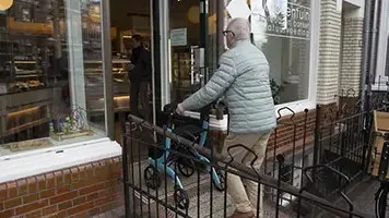 Oudere man loopt ergens binnen met een rollator