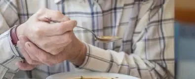 Man houdt lepel vast met soep en ondersteunt met andere hand