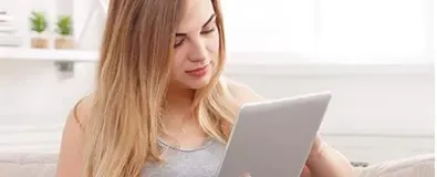Jonge vrouw zit in lichte kamer en bekijkt iets aandachtig op een tablet