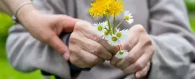 Persoon houdt hand vast van oudere met witte en gele bloemen in de hand