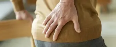 Oudere met hand op heupt die steunt op een stoel