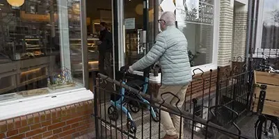 Oudere man gaat een bakkerij binnen met zijn blauwe travixx rollator