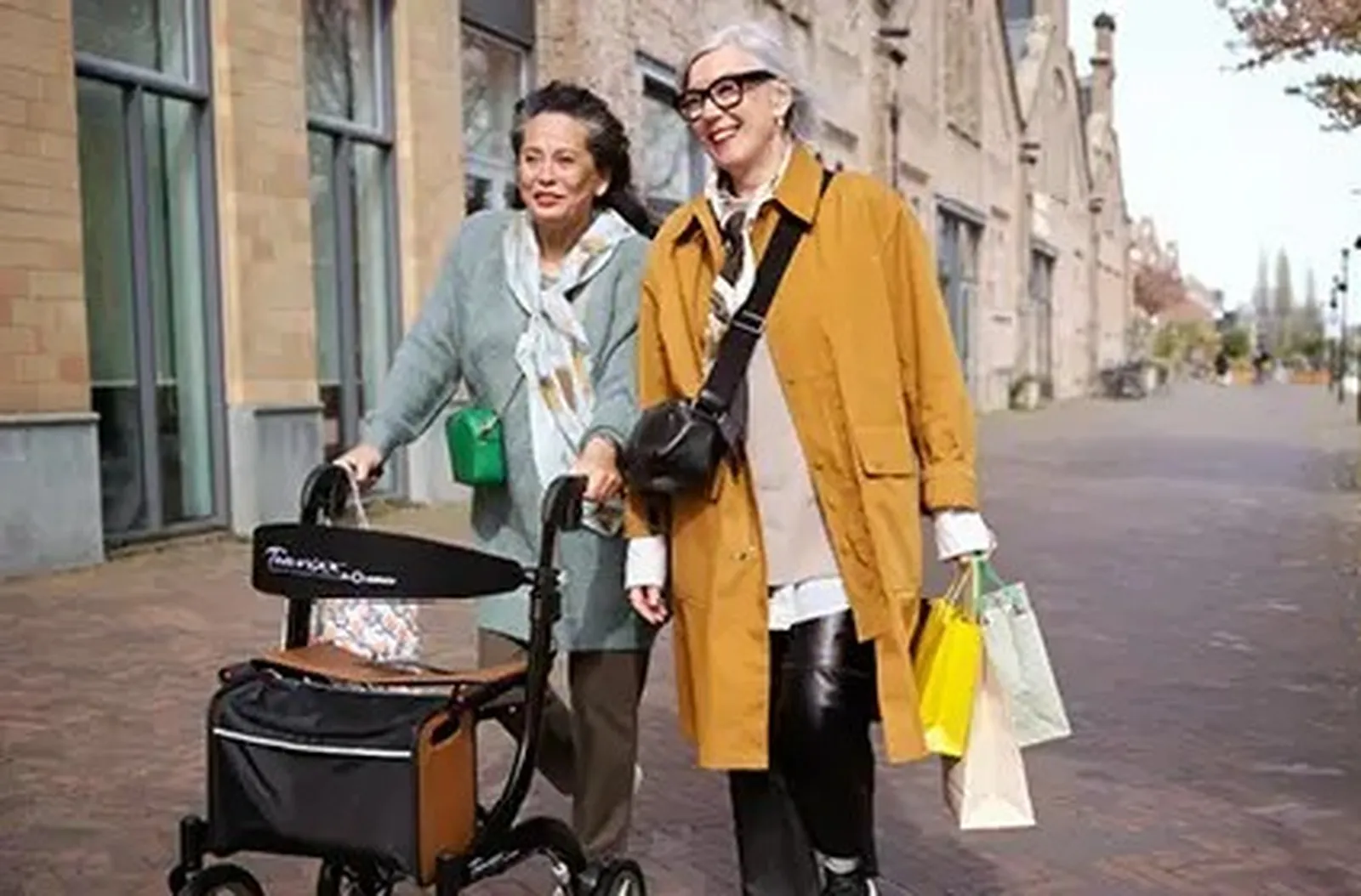 Twee blije vrouwen die door een straat lopen met tassen van winkels en een rollator
