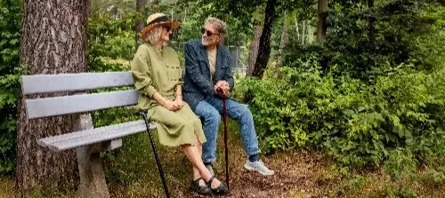 Man en vrouw met wandelstokken opgewekt op een bankje in het bos