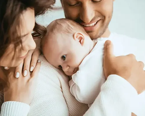 Een man en vrouw glimlachen terwijl ze een baby vasthouden, stralend van blijdschap en liefde voor hun gezin.
