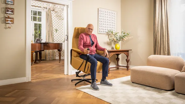 Oudere meneer gebruikt zijn sta-opstoel in de woonkamer. De stoel staat omhoog