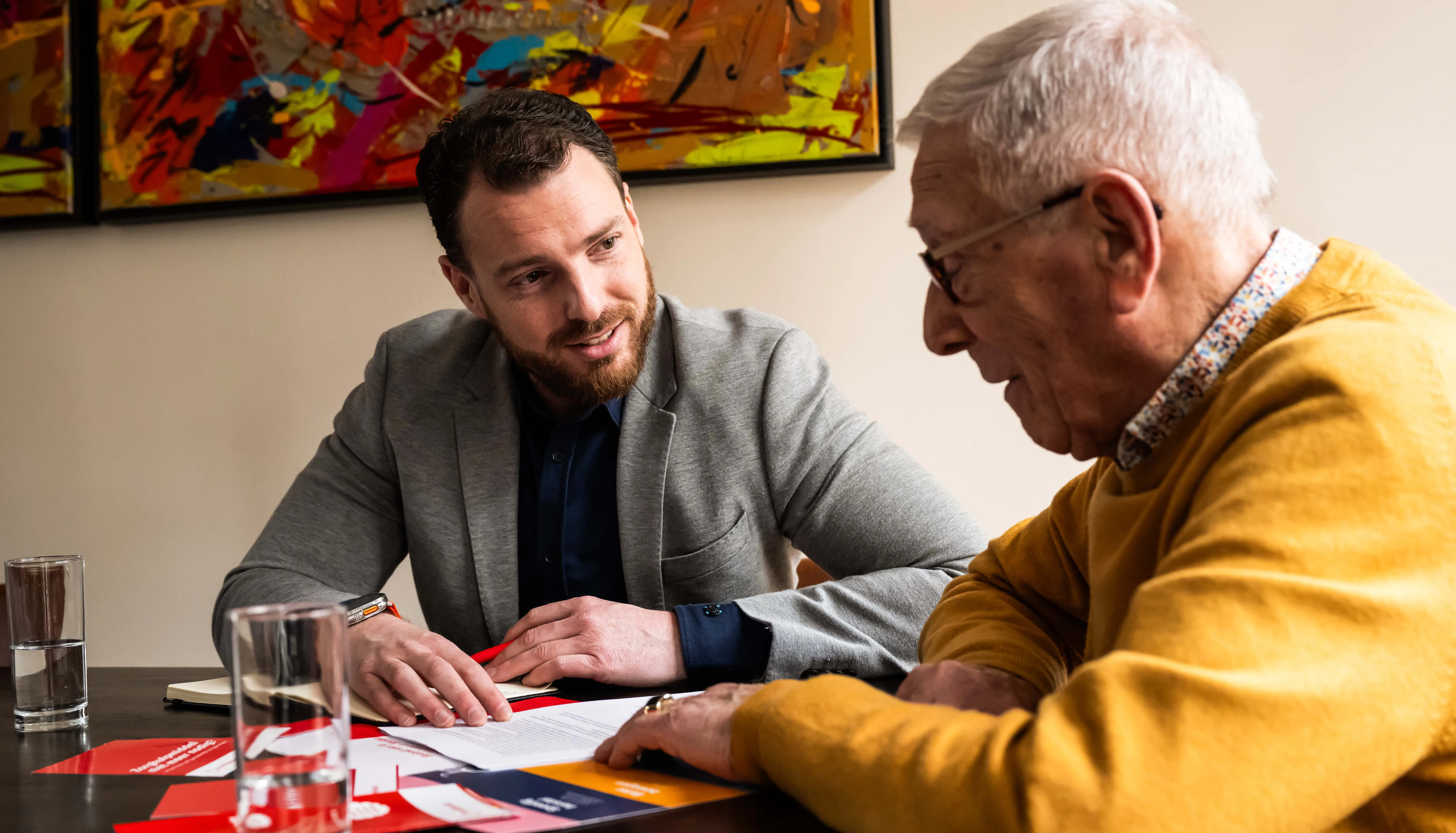 Een thuisadviseur geeft thuisadvies aan een klant. Ze bespreken de papieren die op tafel liggen