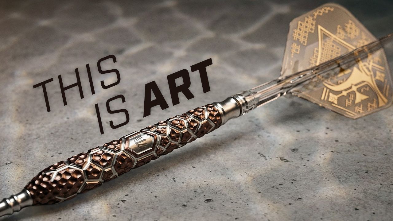 A intricately designed dart with a patterned metallic grip lies on a textured surface. The text reads "This is art."