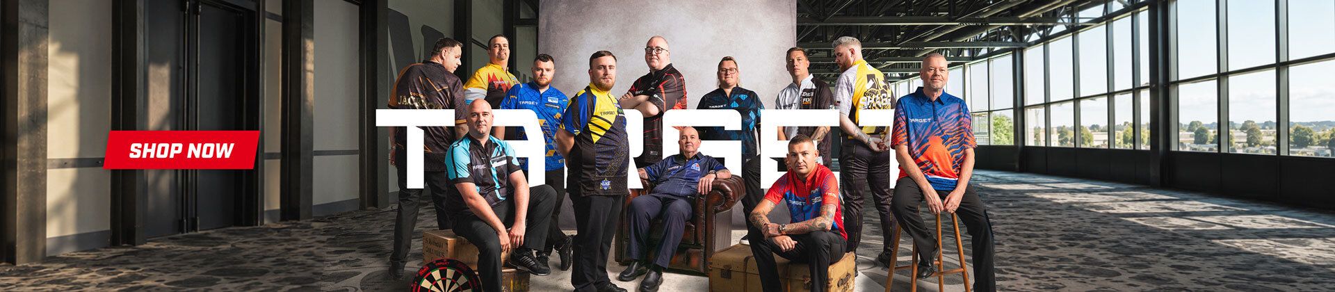 A group of men in colorful dart jerseys posed in a room with large windows. A dartboard is on the floor, and a "Shop Now" button is prominent.