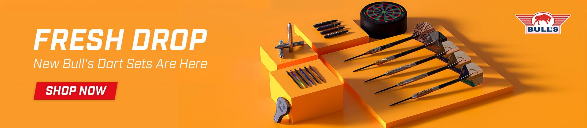 Orange display showcasing six darts, dartboard, and accessories. Text reads "Fresh Drop: New Bull's Dart Sets Are Here" with a "Shop Now" button.