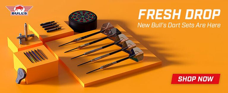 Orange display showcasing six darts, dartboard, and accessories. Text reads "Fresh Drop: New Bull's Dart Sets Are Here" with a "Shop Now" button.
