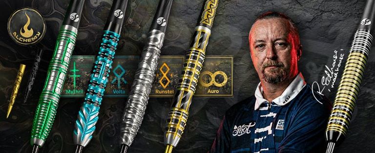 Ritchie Edhouse in a blue shirt stands next to a display of colorful Shot dart barrels with intricate designs, against a dark background with alchemical symbols.
