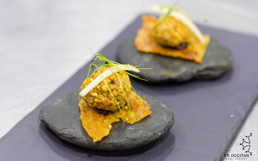 Two bite-sized croquettes on crispy crackers, served on dark slate stones and topped with thin herb garnish.