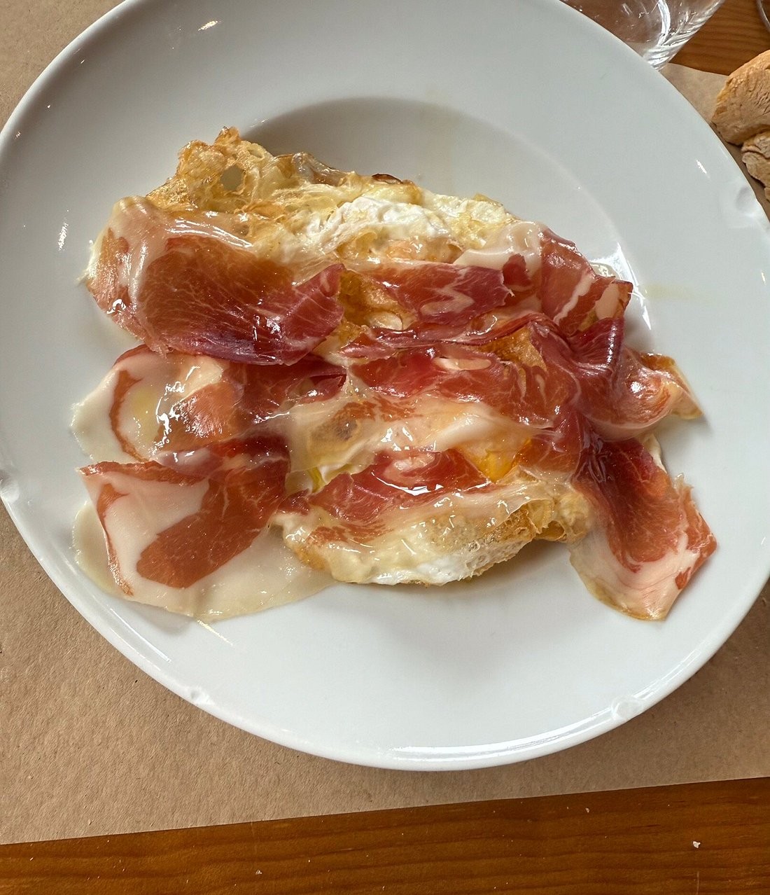White plate with fried eggs topped with thin slices of jamón, with crusty bread on the side.