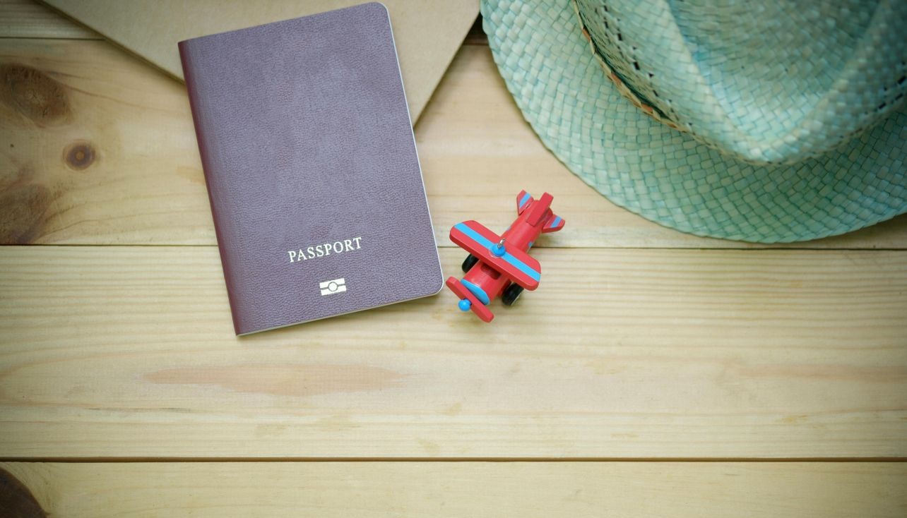 Passport, toy airplane, and green straw hat on a wooden surface suggest travel or vacation plans.