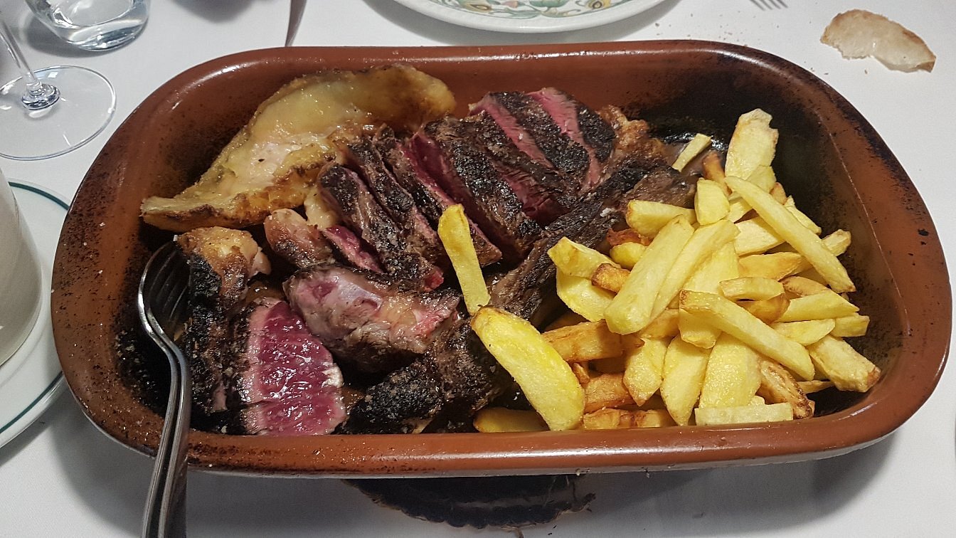 Brown baking dish with sliced medium-rare steak, a roasted potato wedge and a heap of golden fries.