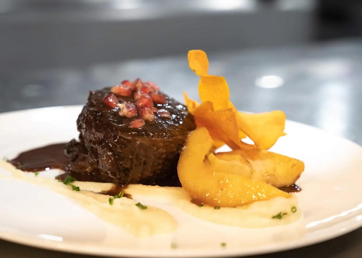 Braised short rib in glossy sauce topped with pomegranate seeds, roasted pear and crisp vegetable chips on a creamy puree.