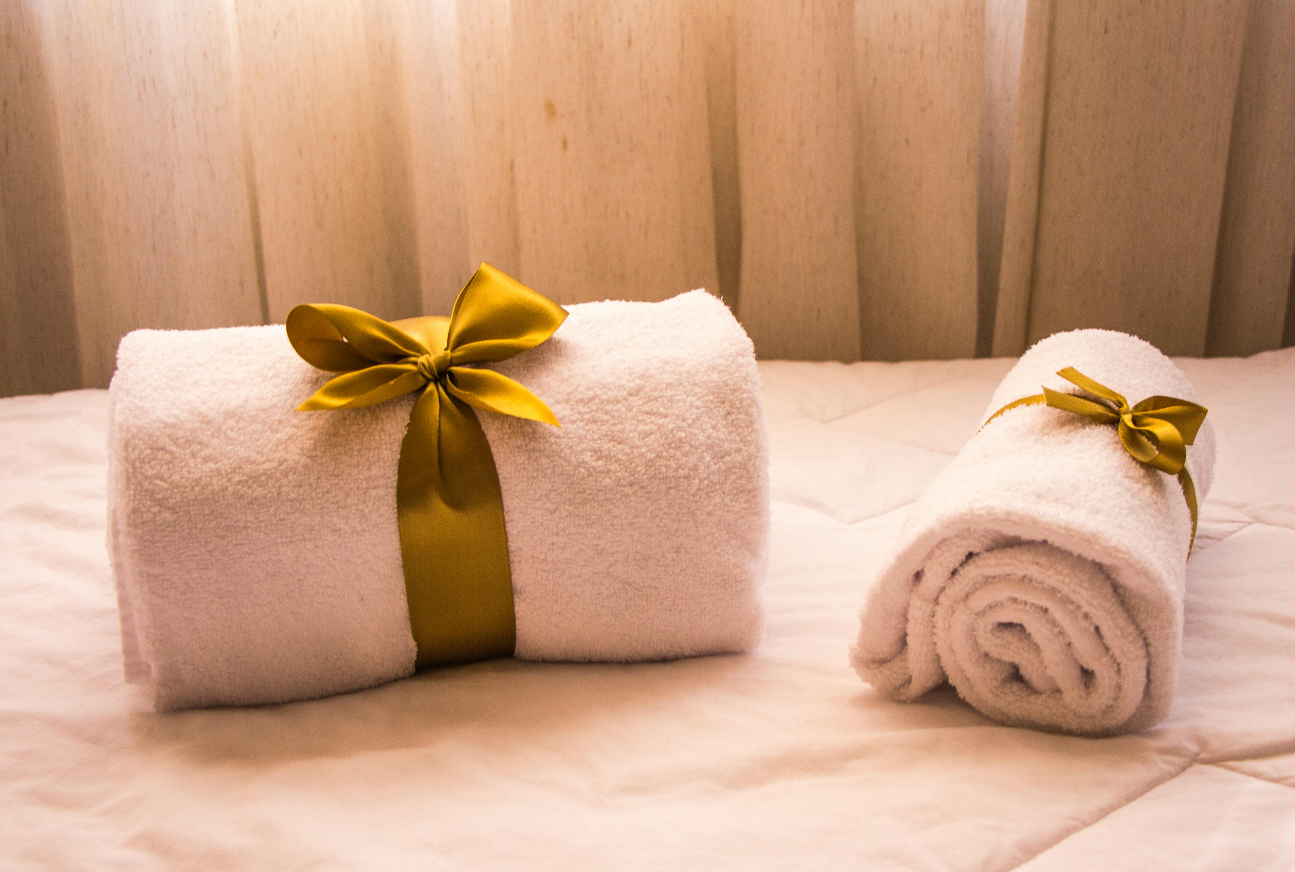 Two white rolled towels on a bed, tied with gold satin ribbons. Soft lighting creates a cozy and inviting atmosphere.