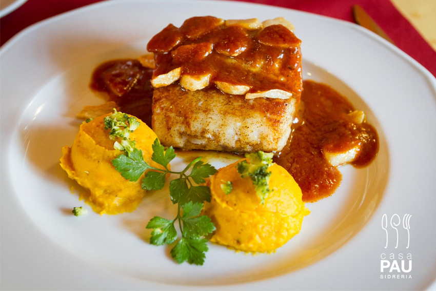 Seared fish fillet topped with sliced almonds and rich brown sauce, served with two orange mashed vegetable scoops and parsley on a white plate.