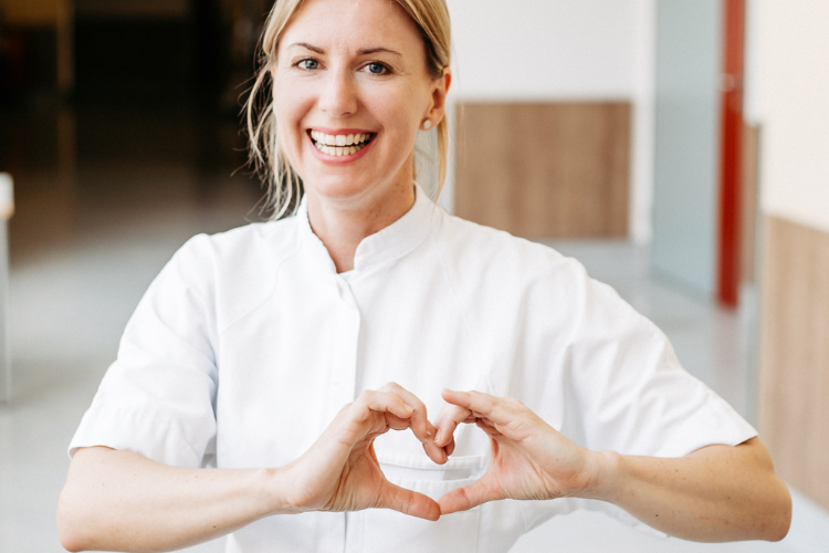 Fröhliche DGKP formt ein Herz mit ihren Händen. 