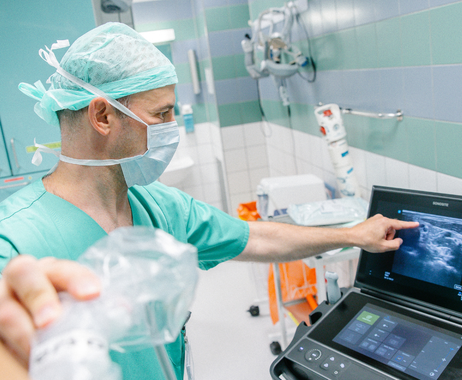 Ein Arzt betrachtet ein Ultraschallbild auf einem Monitor und zeigt auf eine Stelle, während er den Schallkopf in der Hand hält.