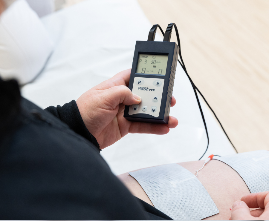 Eine Person hält ein TENS-Gerät für die Heimtherapie in der Hand. Elektroden sind am Bein befestigt und geben elektrische Impulse zur Schmerzbehandlung ab.