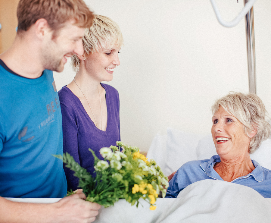 Eine ältere Frau und ein junger Mann lächeln während eines Krankenhausbesuchs.