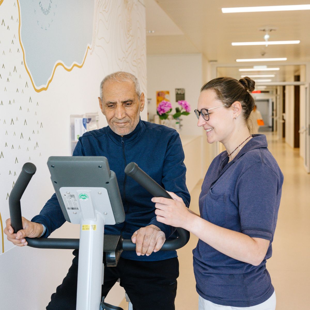 Eine Physiotherapeutin berät einen Patienten der Onkologie, der auf einem Ergometer sitzt.