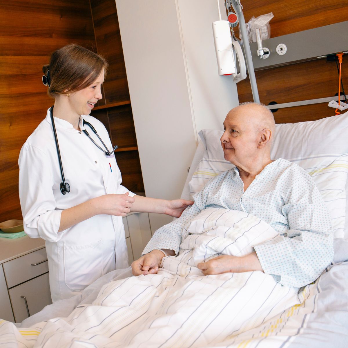 Eine Ärztin im Gespräch mit einem älteren Patienten, der im Bett liegt.