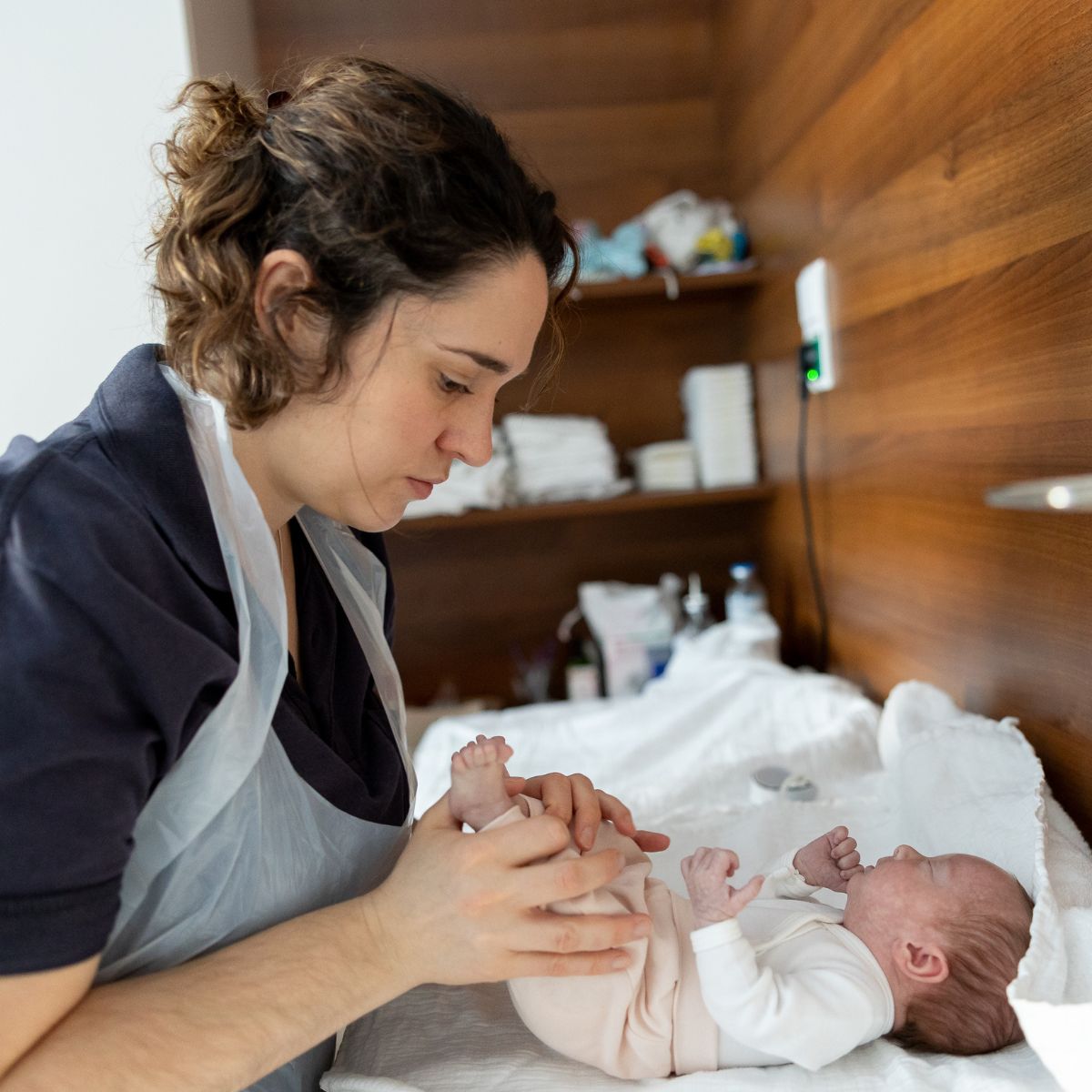 Eine Physiotherapeutin bewegt ein Neugeborenes an den Beinen. Das Neugeborene liegt auf einer Unterlage vor ihr.