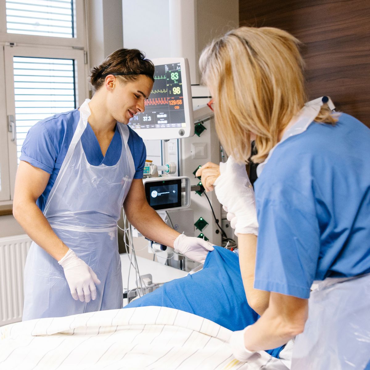 Zwei Pflegepersonen auf der Intensivstation lagern gemeinsam einen Patienten im Bett um.