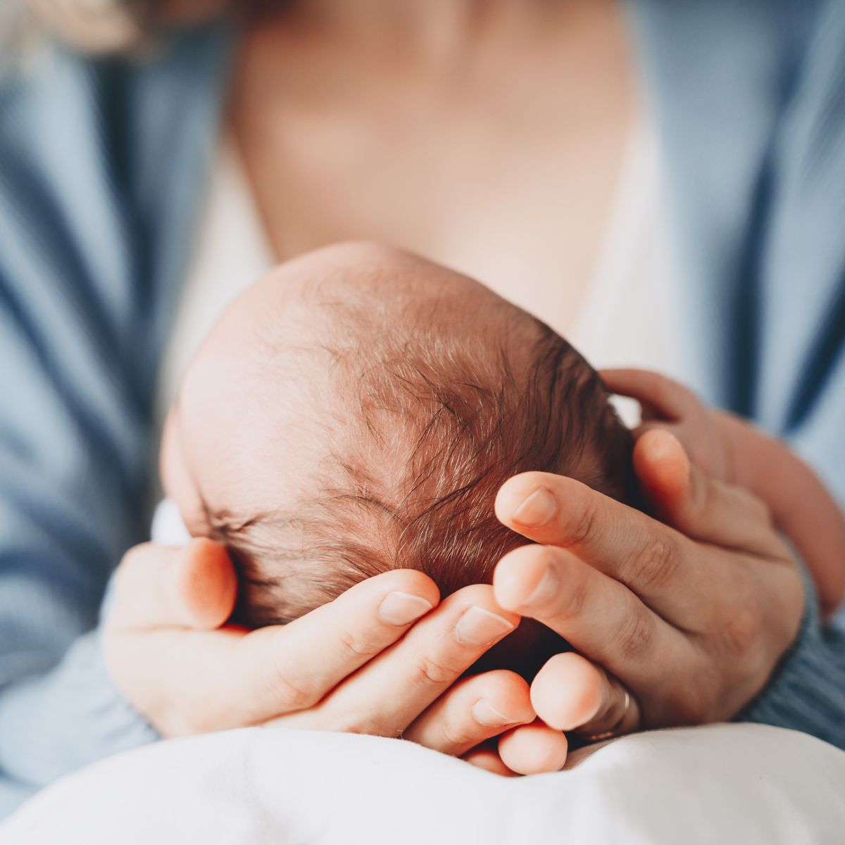 Ein Baby liegt mit dem Köpfchen in den Händen der Mutter.