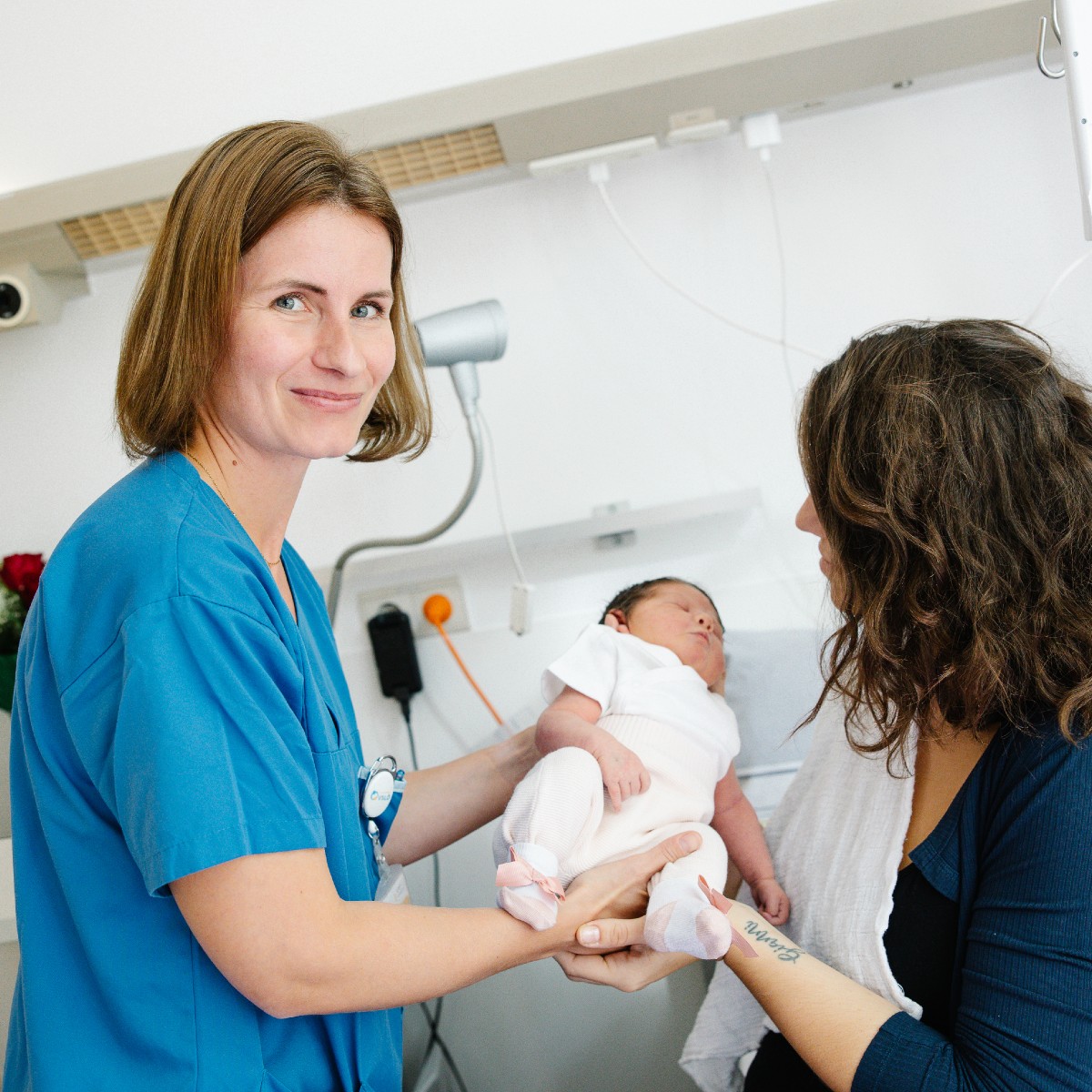 Eine Pflegekraft zeigt einer Mutter den Umgang mit ihrem Neugeborenen. 