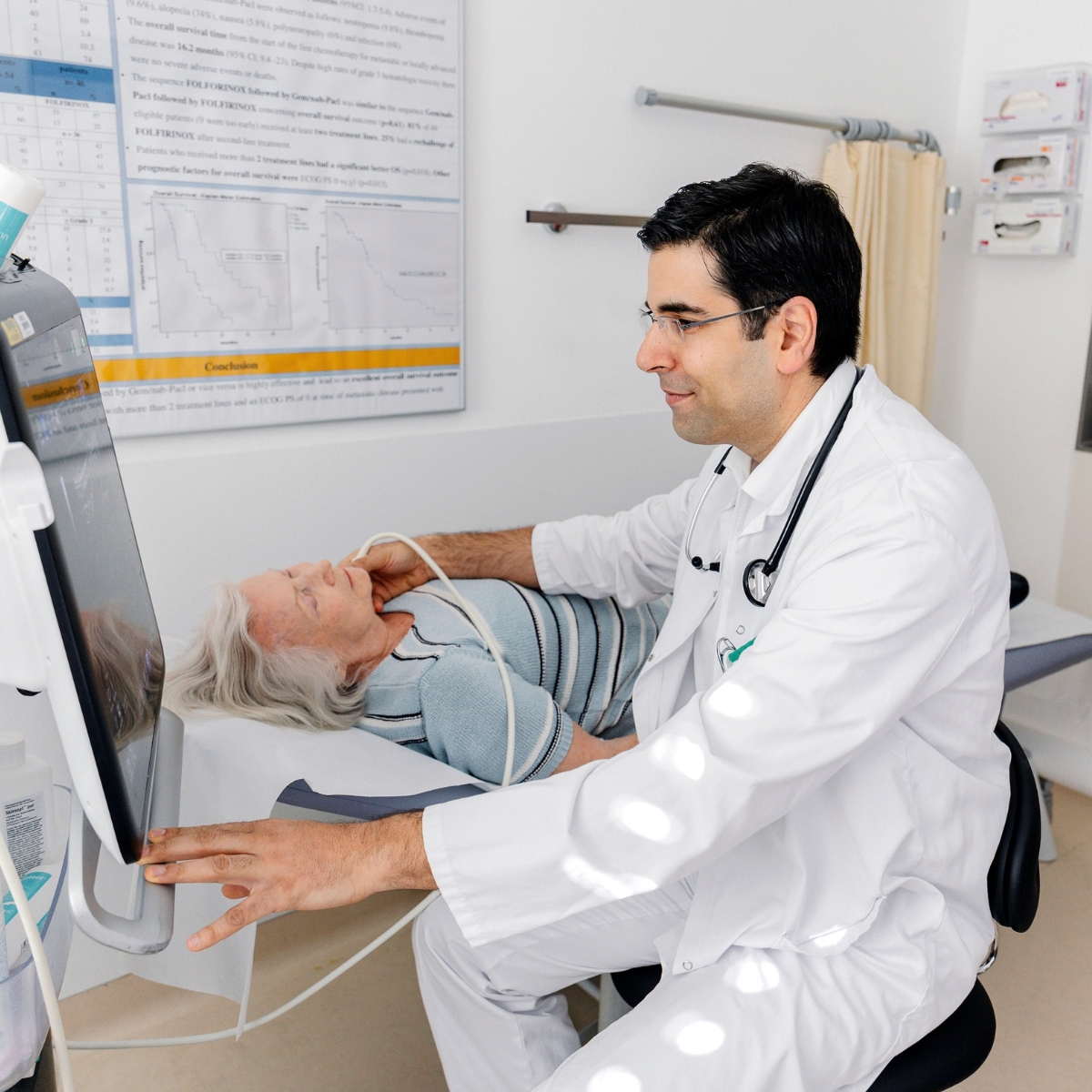 Ein Arzt sitzt neben einer liegenden Patientin und macht einen Ultraschall am Hals.