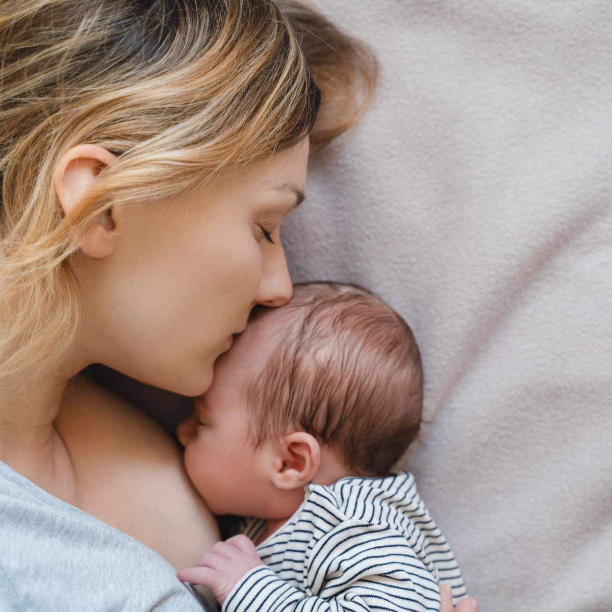 Eine Mutter stillt ihr Baby im Bett und küsst es.