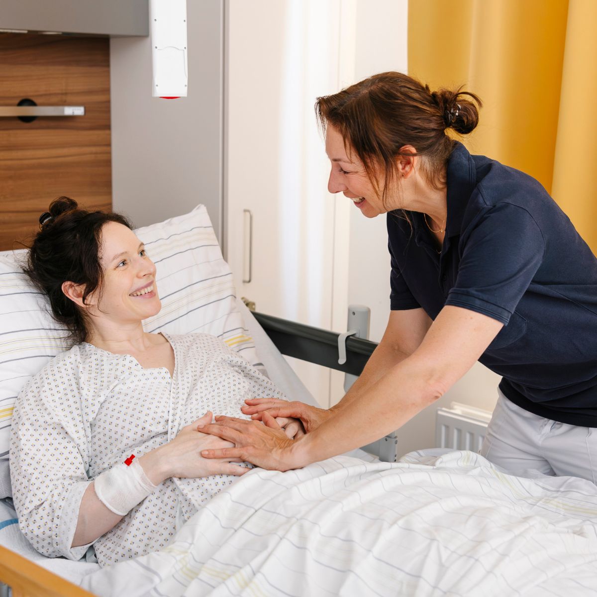 Eine Physiotherapeutin berät eine Patientin, die nach der Geburt im Bett liegt, zu Rückbildungsübungen.