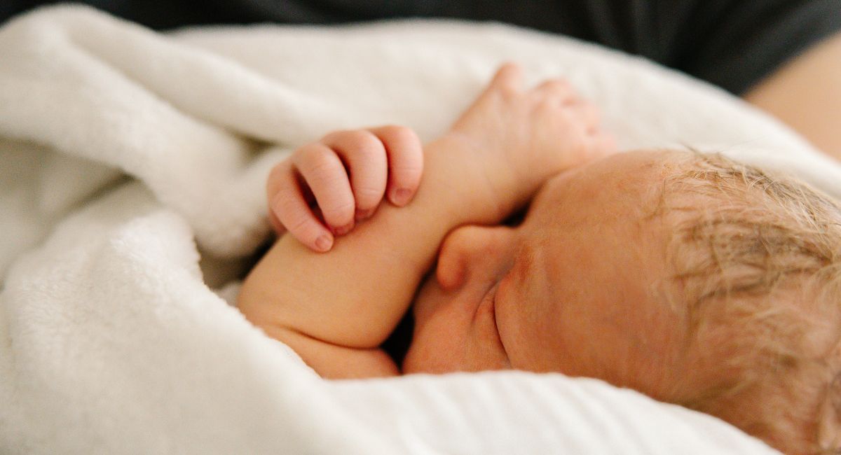 Ein Neugeborenes liegt eingewickelt in eine weiße Decke im Arm seiner Mutter.