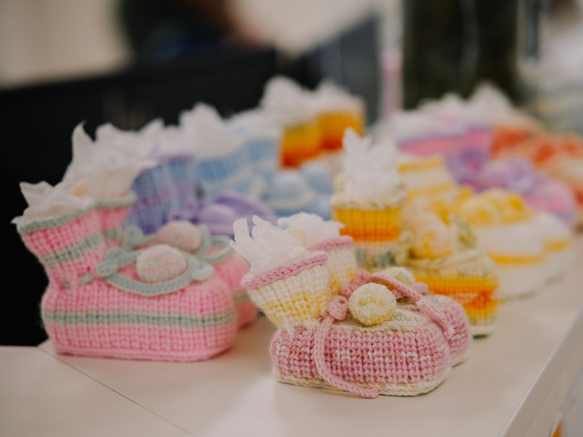 Viele gestrickte Babyschuhe stehen nebeneinander aufgereiht.