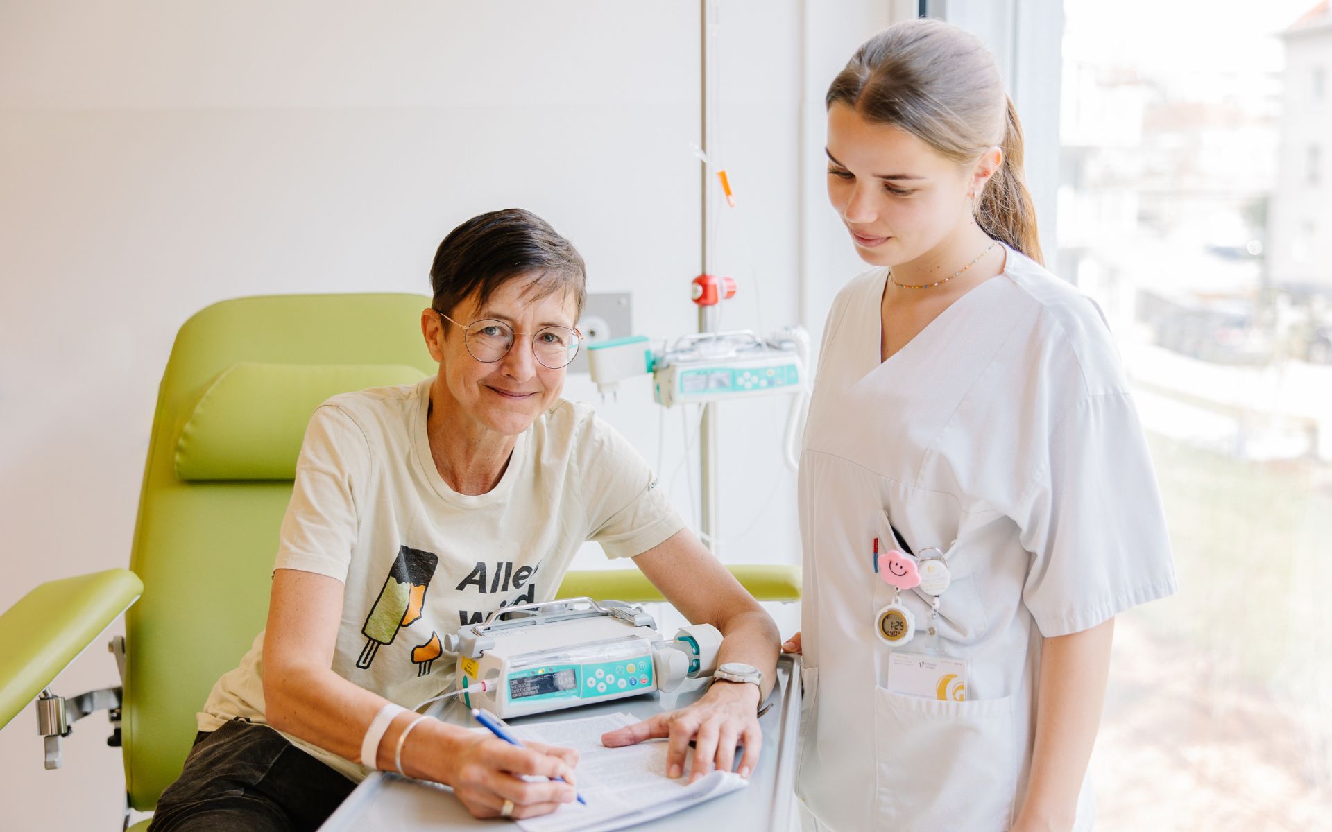 Eine Krebspatientin sitzt bei der Chemotherapie und füllt mit der Hilfe einer Krankenpflegerin ein Formular aus.