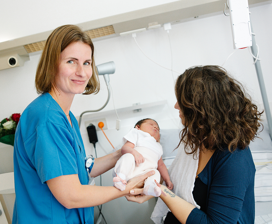 Eine Pflegekraft zeigt einer Mutter den Umgang mit ihrem Neugeborenen.