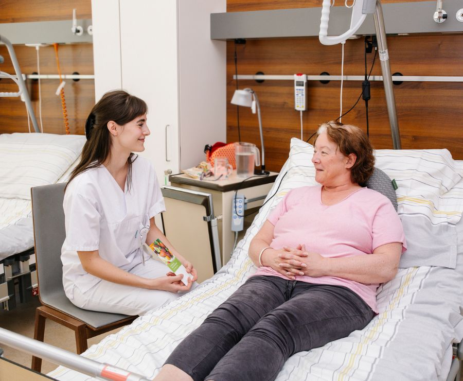 Eine Diätologin im Gespräch mit einer Patientin, die im Bett liegt.