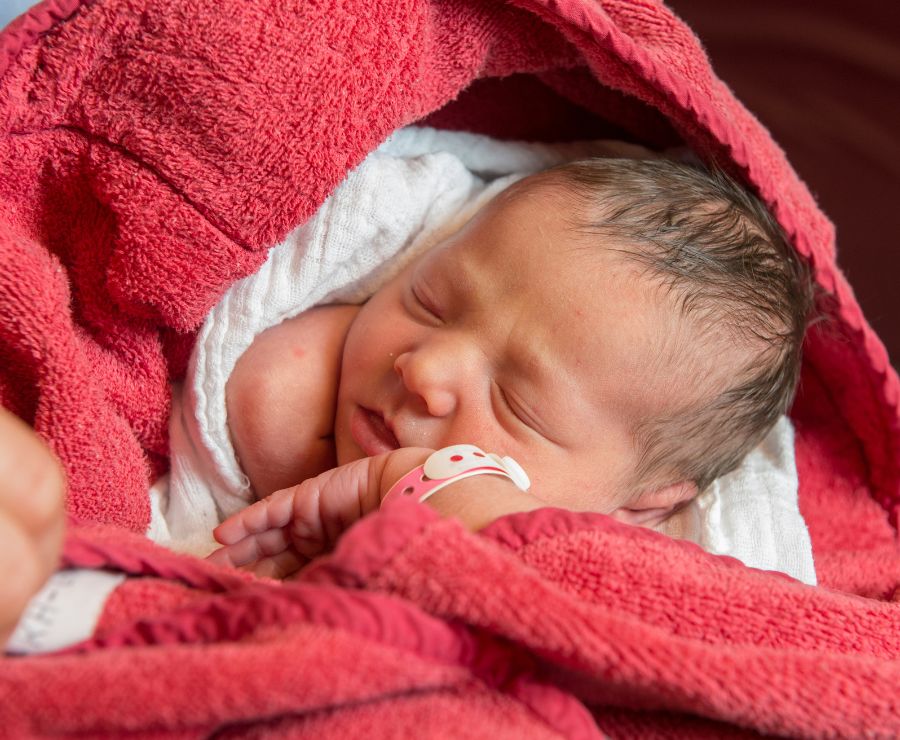 Ein schlafendes Baby ist in ein rotes Handtuch gewickelt.