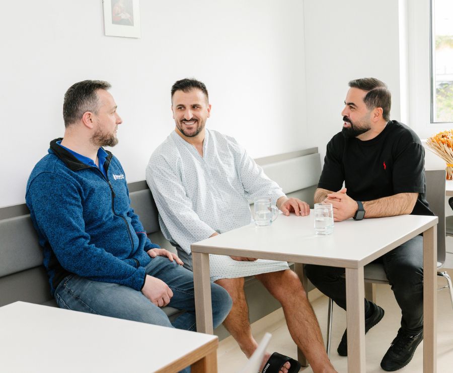 Ein Patient und zwei Besucher sitzen um einen Tisch und unterhalten sich.