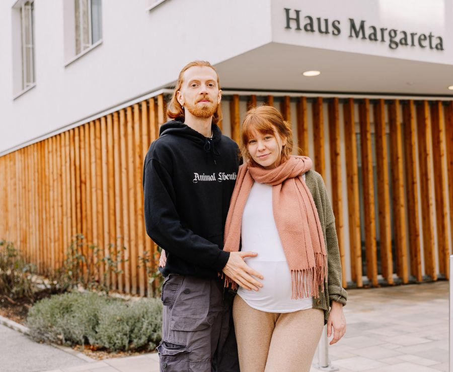 Eine schwangere Frau und ihr Partner stehen vor dem Geburtshaus.