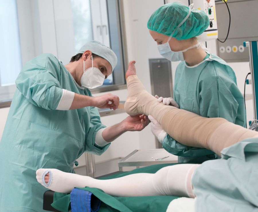Ein Arzt in OP-Kleidung verbindet das Bein eines Patienten.