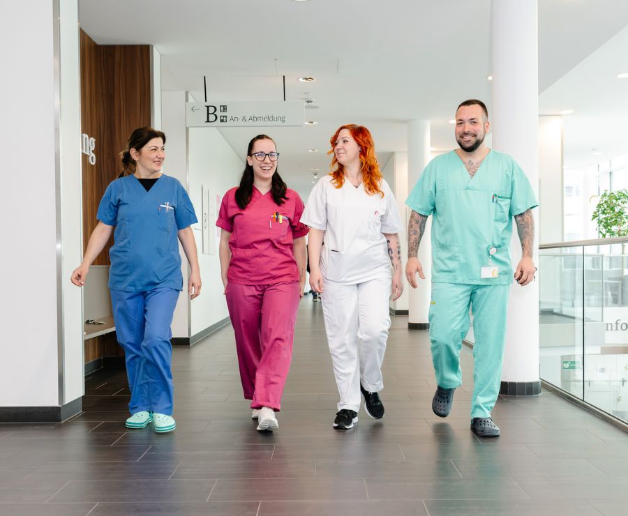 Vier Pflegefachkräfte in unterschiedlichen Farben gehen im St. Josef Krankenhaus Wien über den Flur.