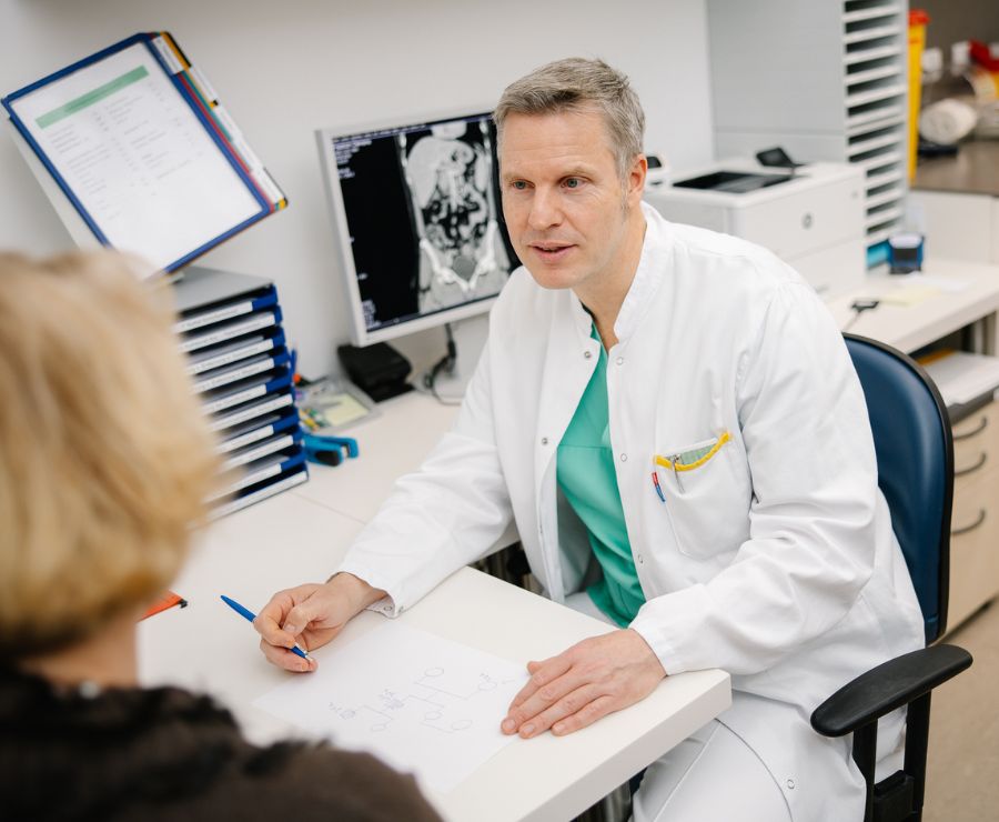 Ein Arzt sitzt mit einer Patientin an einem Tisch und führt ein Gespräch mit ihr.