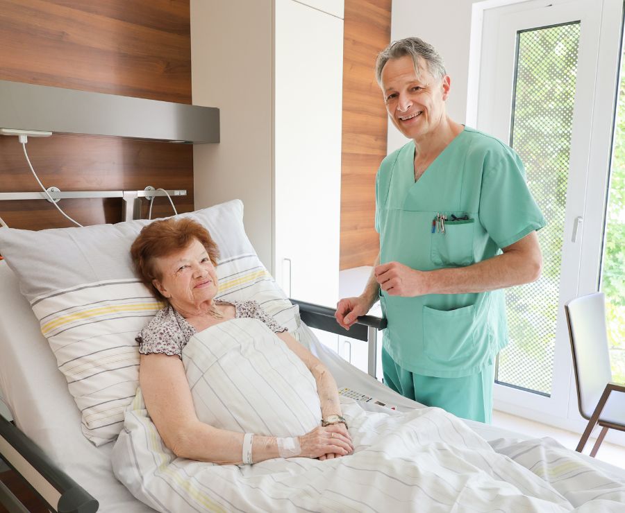 Ein Arzt im Gespräch mit einer Patientin, die im Krankenbett liegt.
