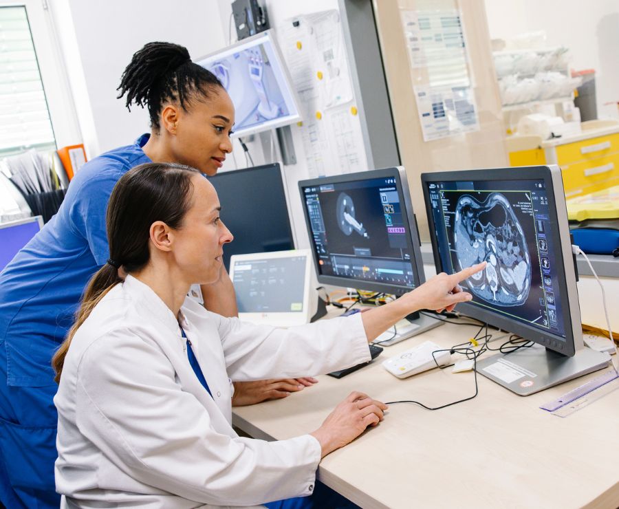 Eine Ärztin und eine Radiotechnologin schauen sich ein CT-Bild auf einem Bildschirm an..